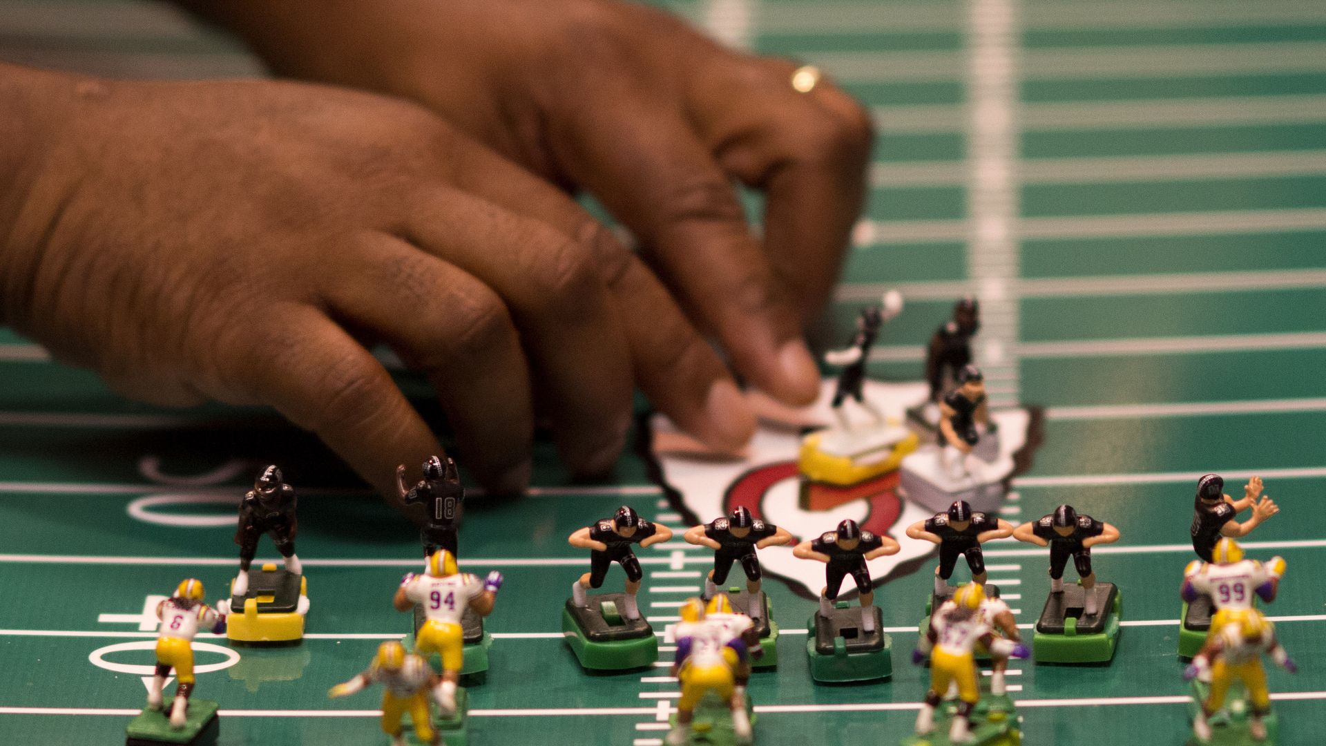 A person adjusts small figures of football players on an electric football game field.