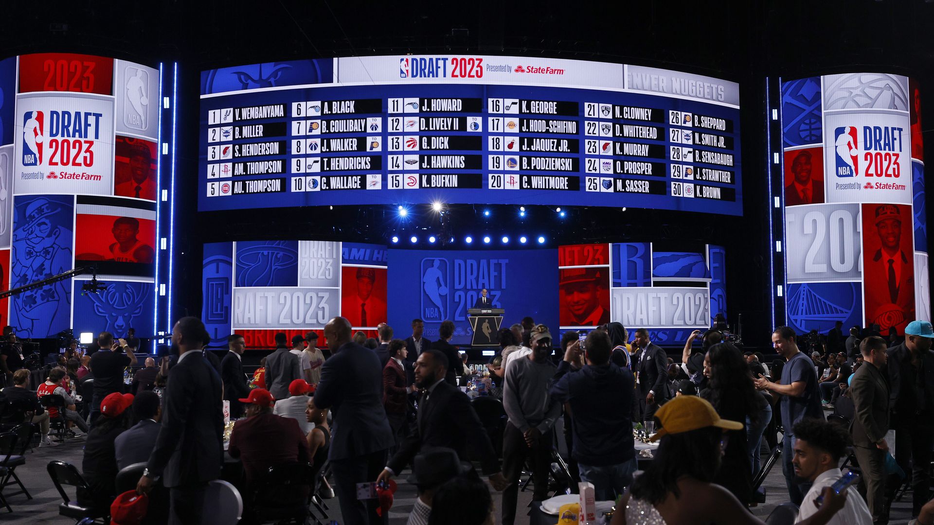 A crow of people gathered in front of a stage with multiple screens showing NBA Draft 2023 information.