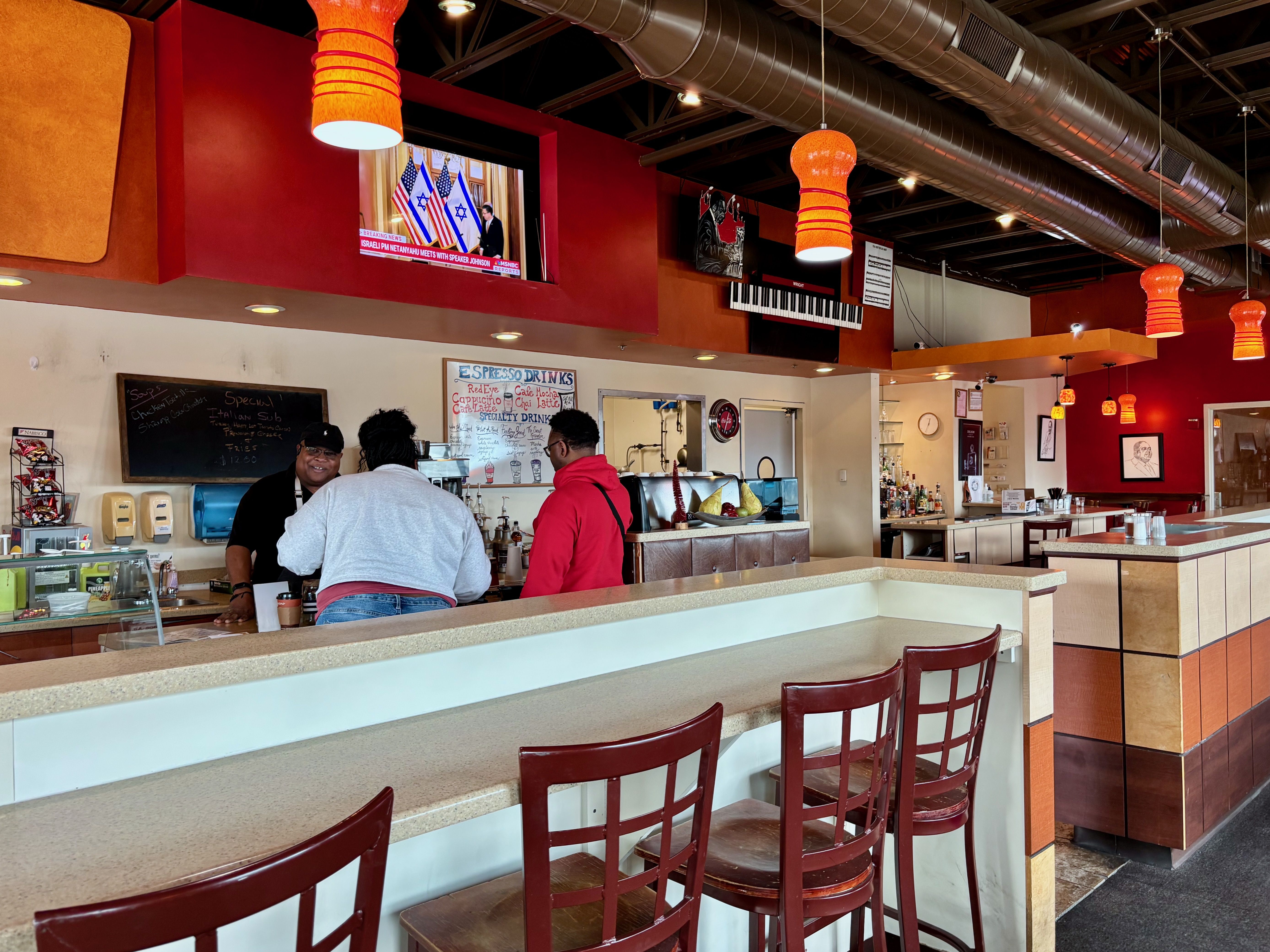 Two people order at the counter at Lincoln Cafe, with a red interior and hanging orange lights