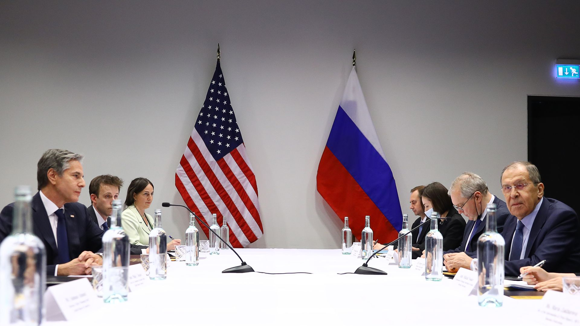 Flags of the U.S. and Russia stand next to a table for a meeting between diplomats.