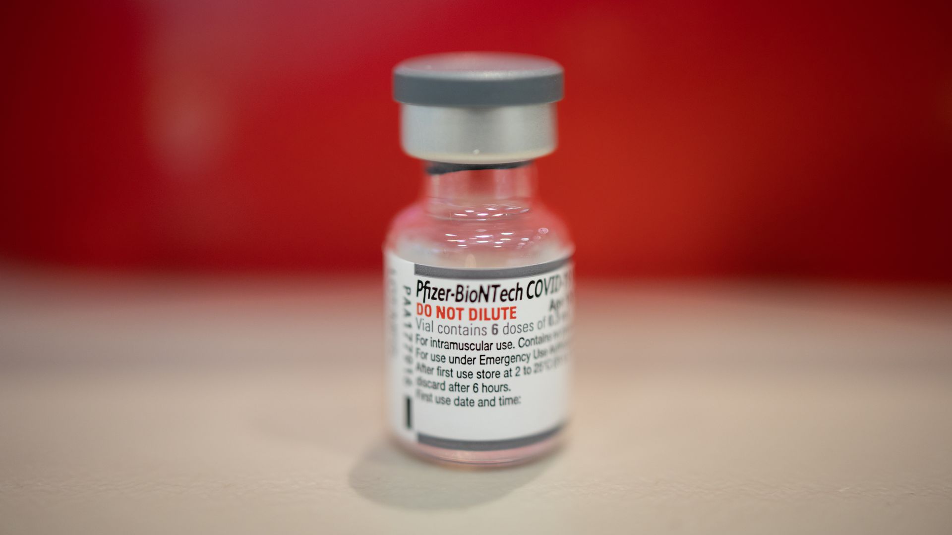 Photo of a vial of the Pfizer-BioNTech vaccine against a red background