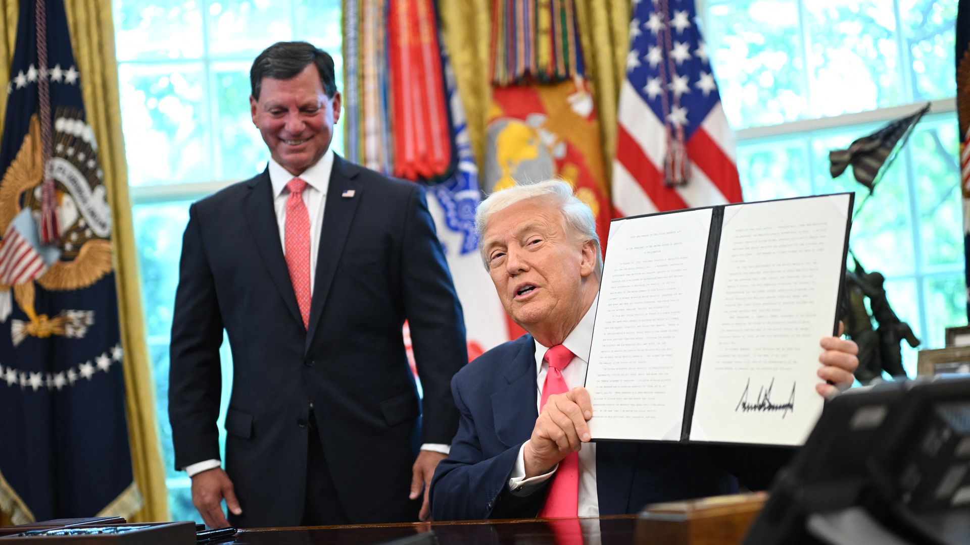 Donald Trump holds a signed presidential proclamation honoring the 90th anniversary of the Social Security Act, joined by Commissioner of the Social Security Administration Frank Bisignano (L) in the Oval Office of the White House. 