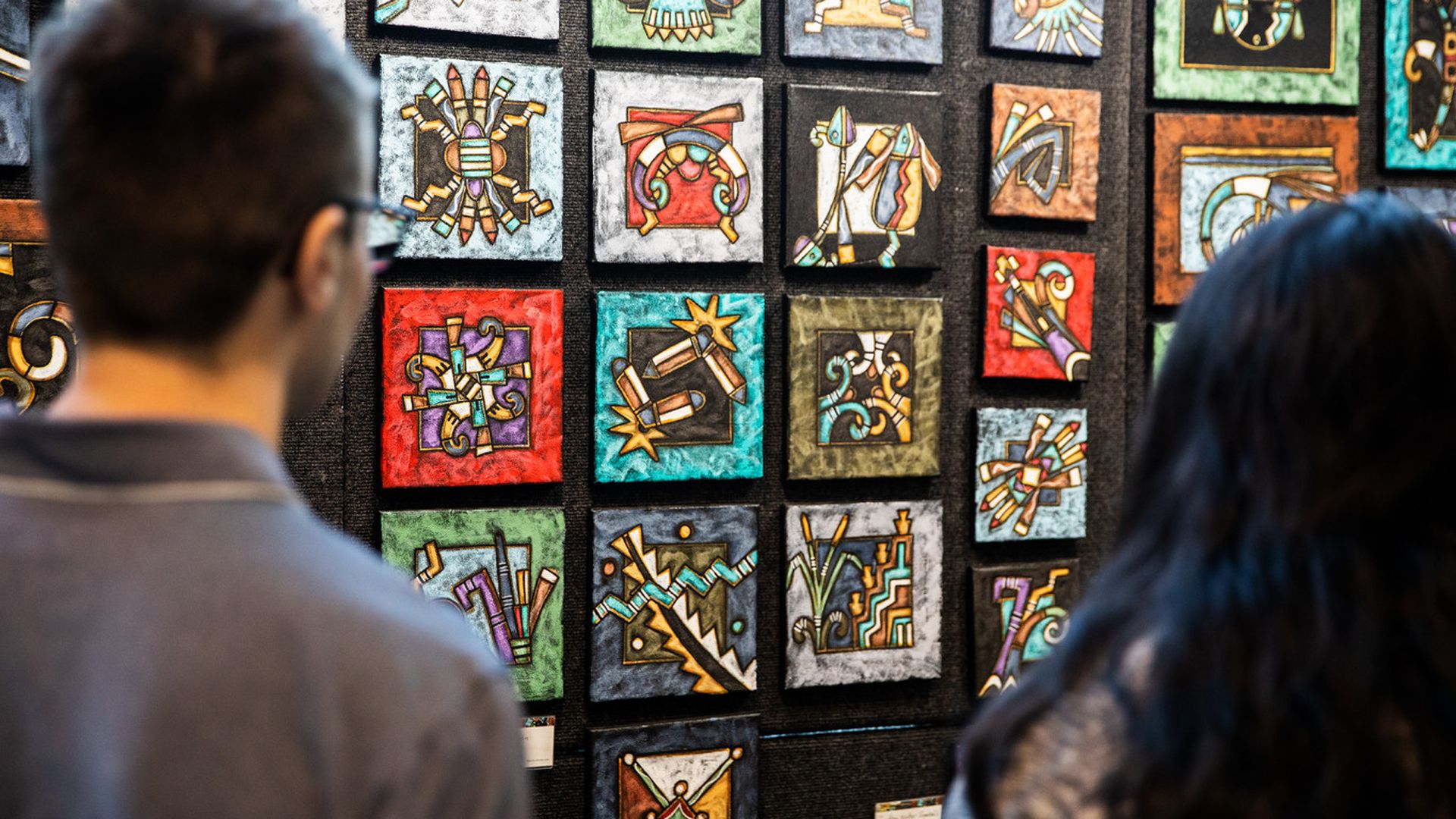 Two people look at colorful tiles at an art show.