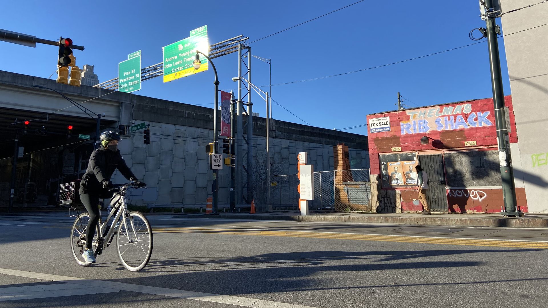 A bicyclists pedals on a street with a vacant building and raised interstate in the background