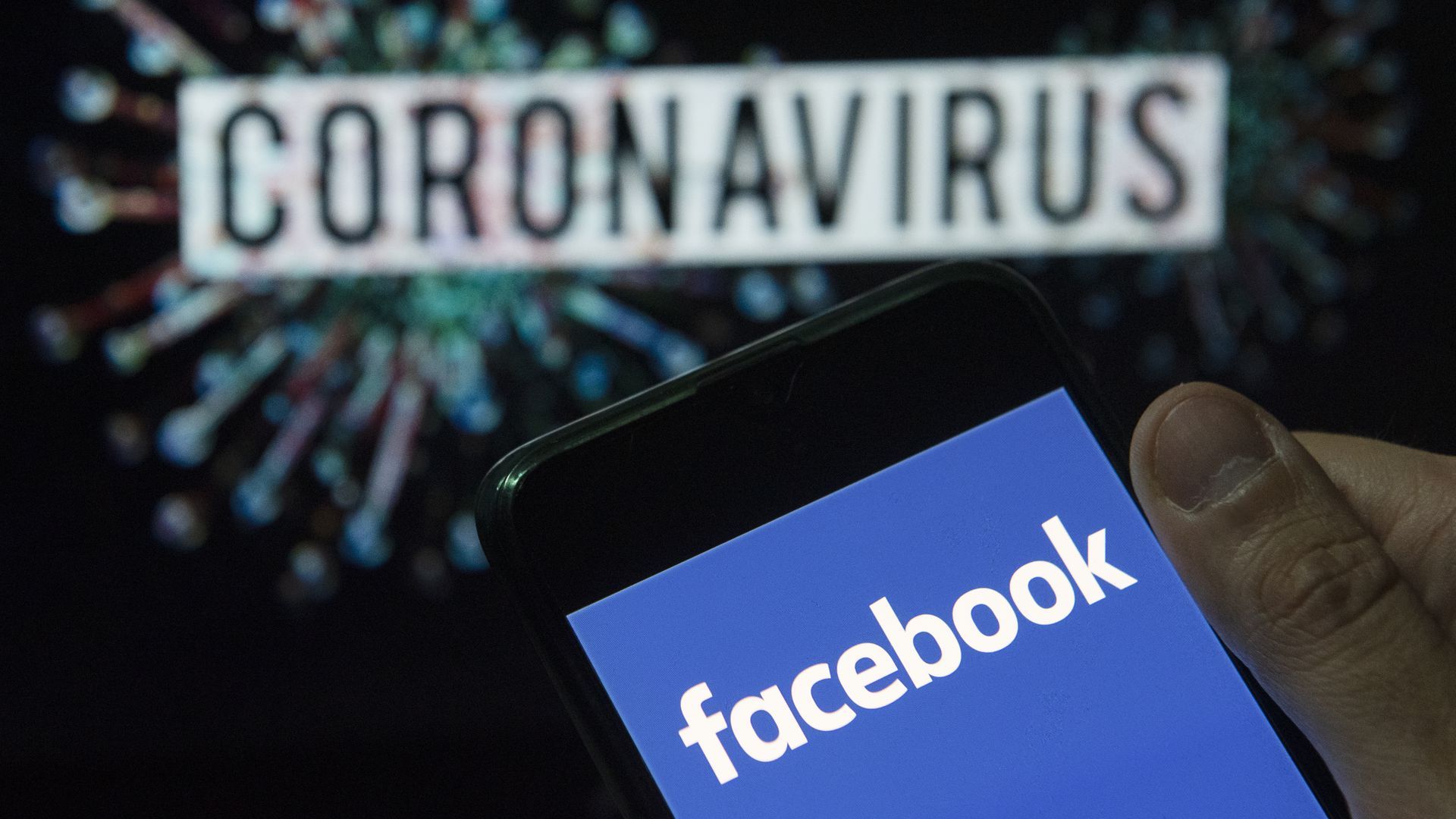 A photo illustration of a Facebook logo on a smartphone in front of a Coronavirus sign.