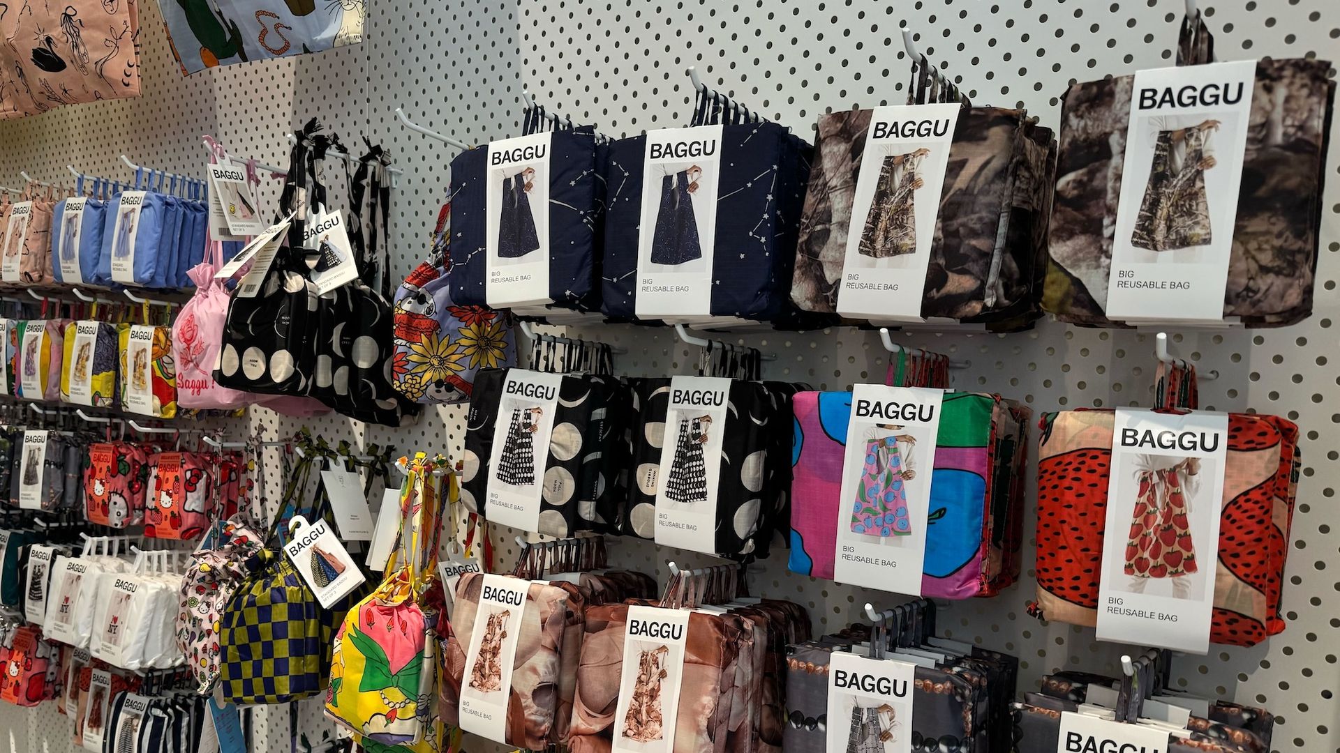 Wall with Baggu bags in different patterns hanging from hooks.