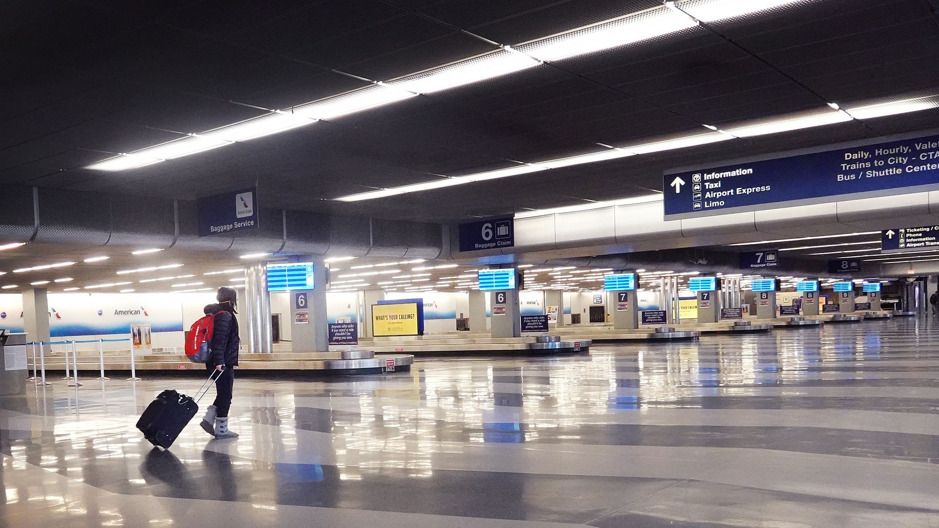 One person pulling a roller suitcase in an empty baggage claim at O'Hare airport.