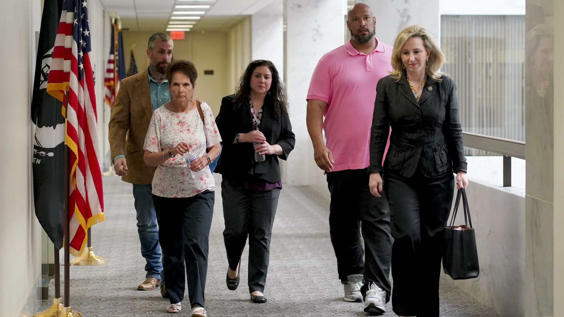 Gladys Sicknick, mother of Brian Sicknick, and Sandra Garza walk down a hallway with several other people