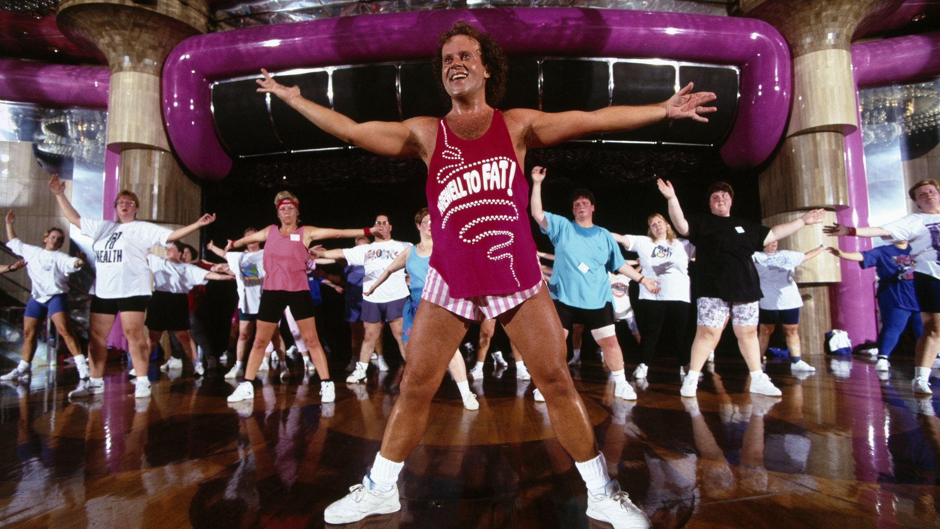 Richard Simmons stands with his arms outstretched as he leads an exercise class.