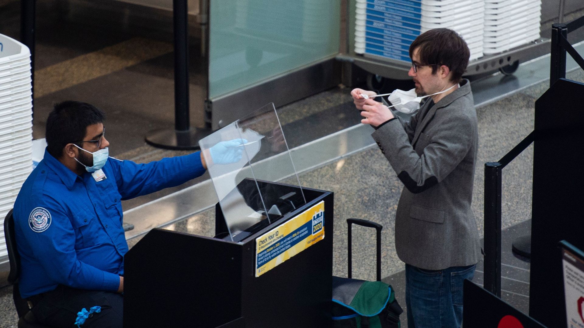 A passenger removes a mask to be checked by a TSA officer.