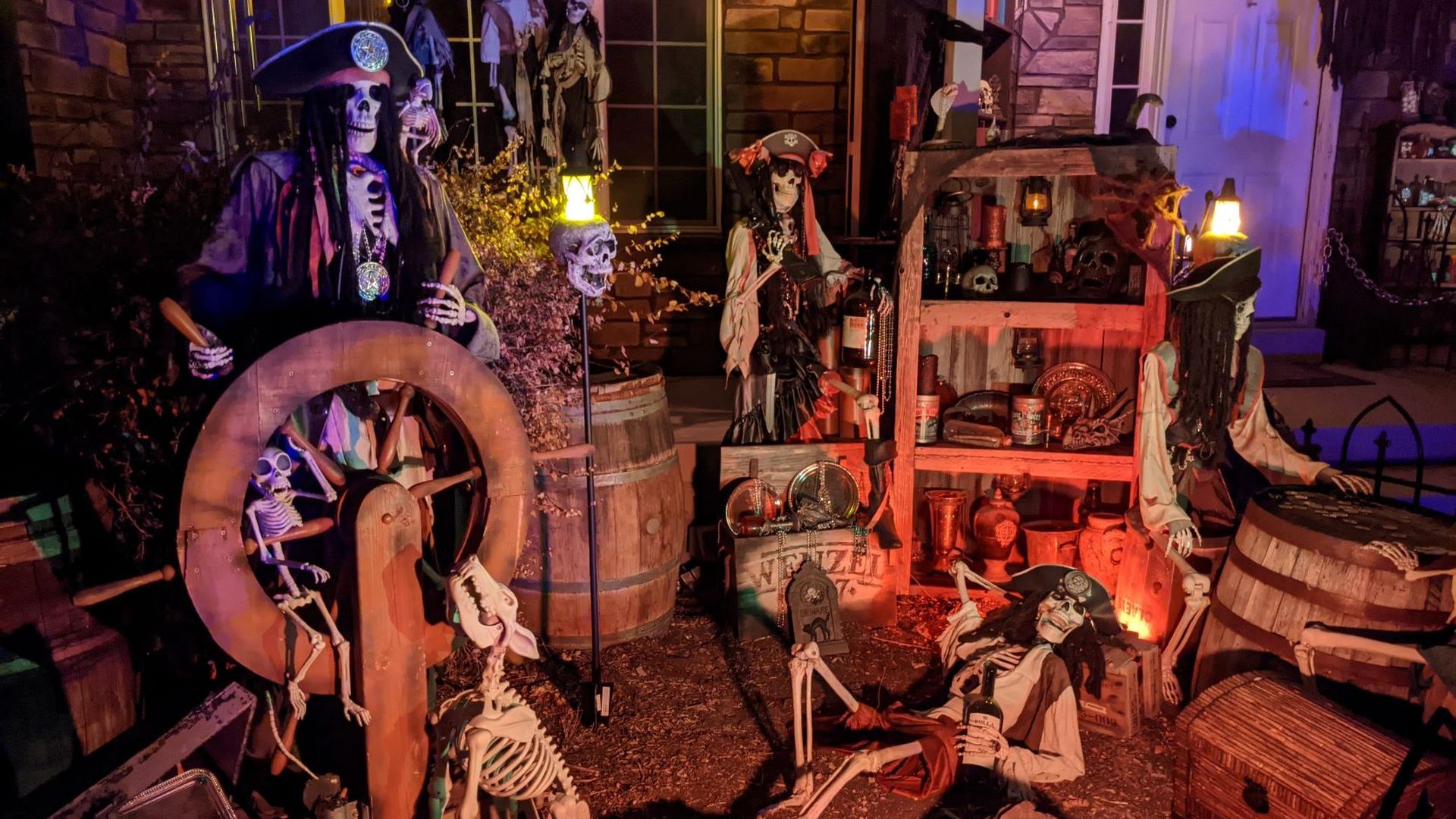 Fake skeletons are posed as pirates around barrels, treasure chests and a captain's wheel in a Halloween display.