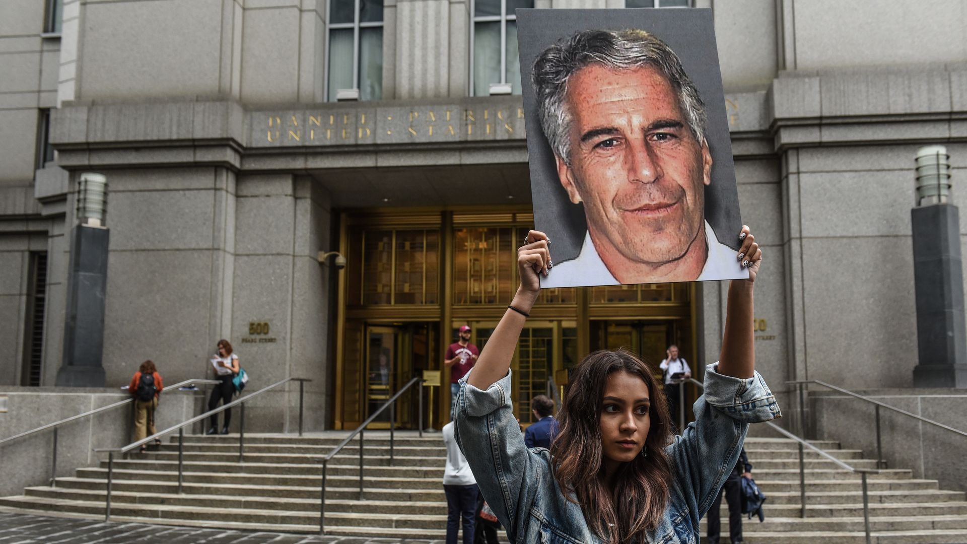 A girl holding up a poster of Epstein's face.