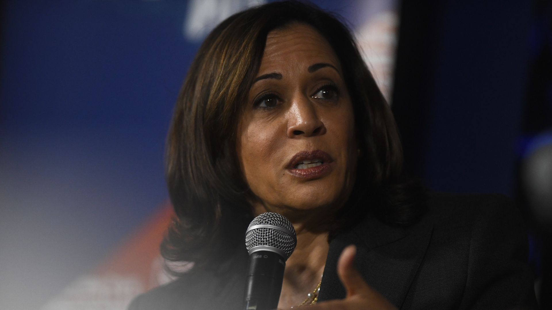 In this image, Kamala Harris speaks into a microphone while wearing a blazer.