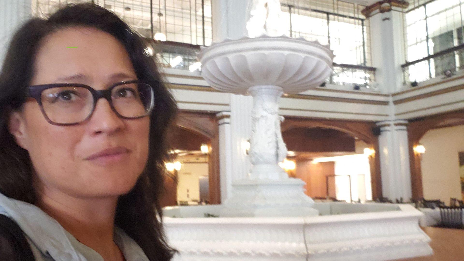 Woman to the left and in front of large white fountain.