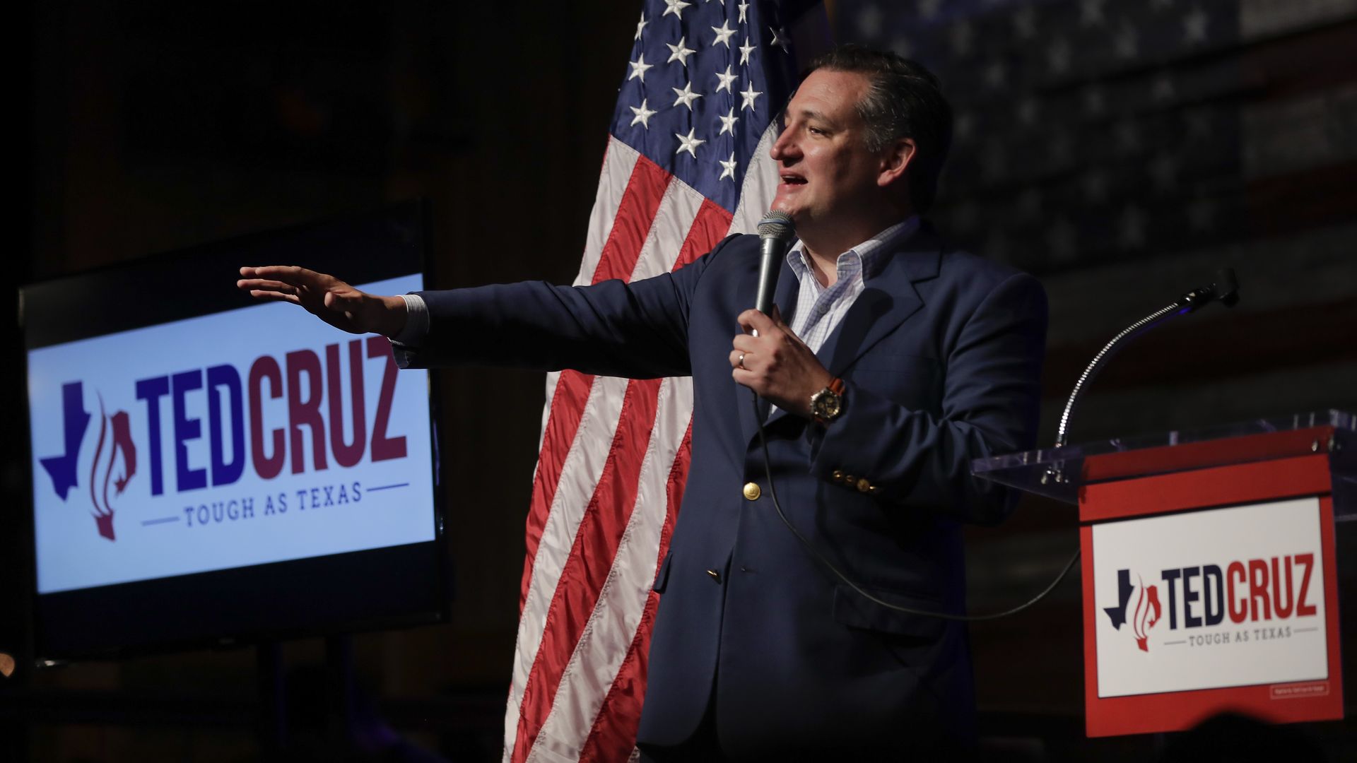 Ted Cruz holding a microphone in one hand and his other arm is outstretched, palm down
