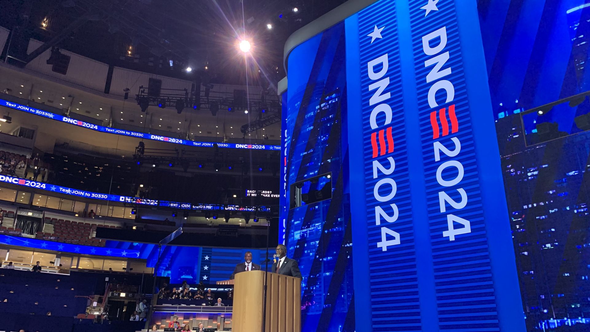 A man behind a podium with a huge banner that says DNC 2024