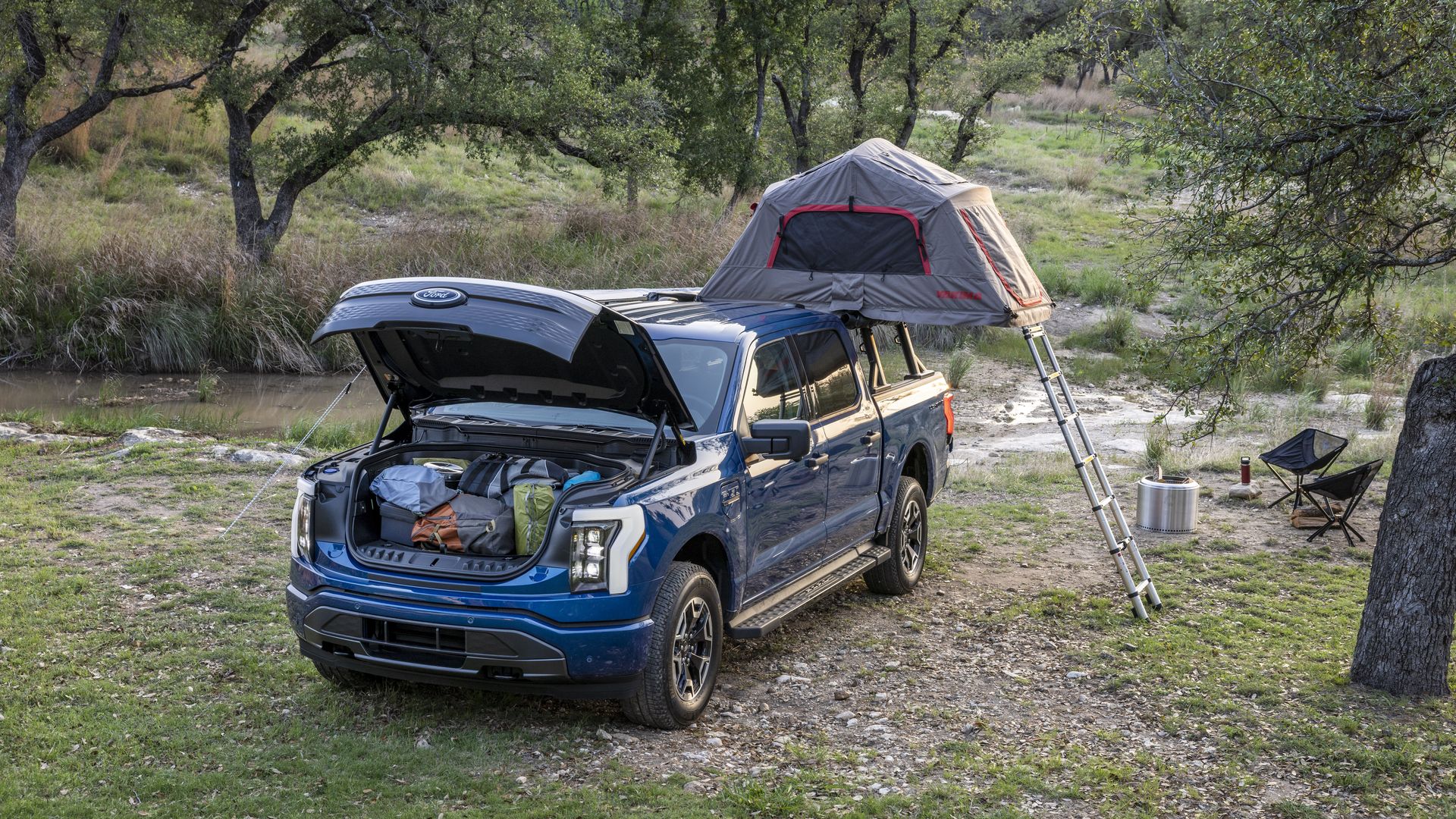 Image of a Ford F-150 Lightning electric pickup with a tent on the roof and the open frunk stuffed with gear. 