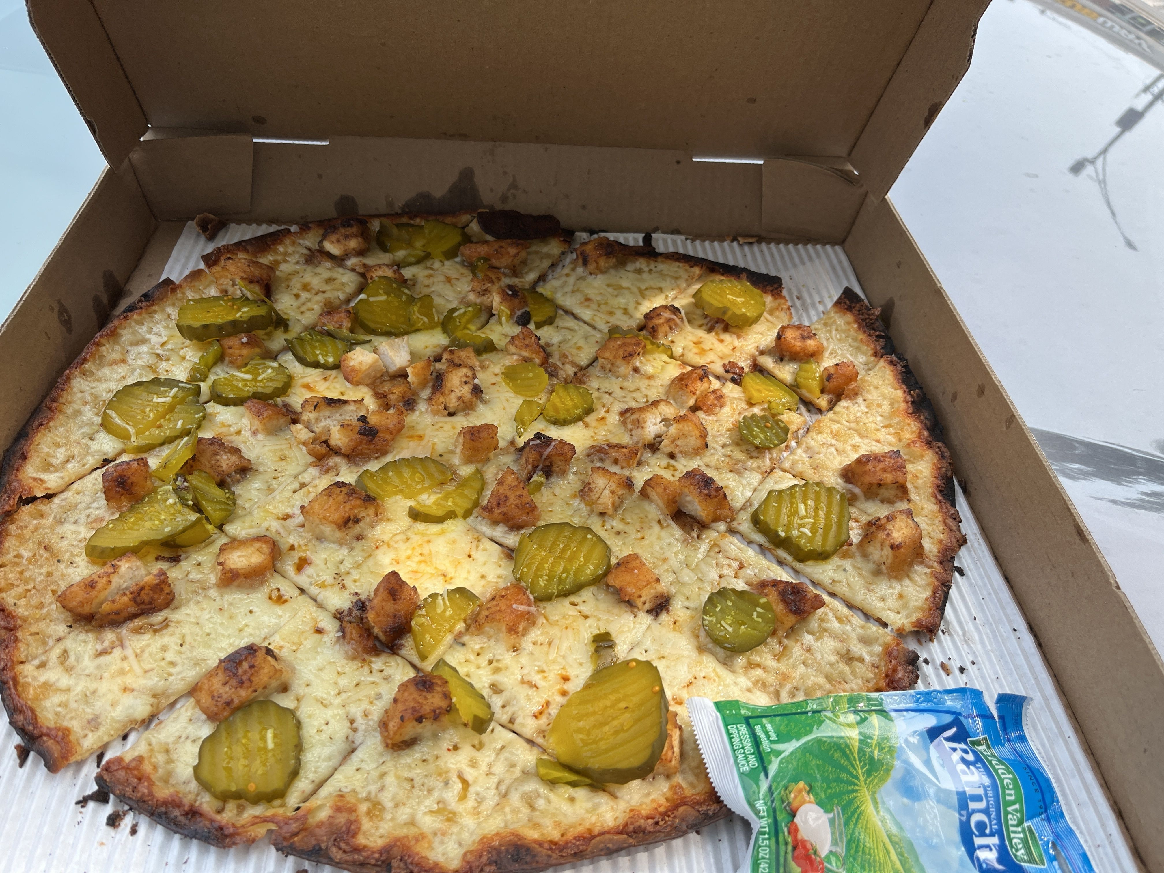 Photo of a pizza with chicken and pickles on it 