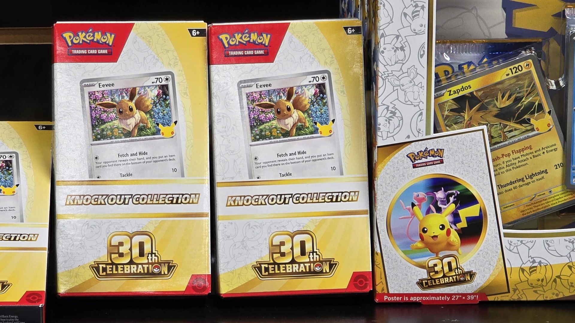 Pokemon trading cards on a store shelf: two Eevee boxes in the center, a Zapdos card near them, and a blue Articuno card on the right, with Pikachu imagery and 30th Celebration graphics.