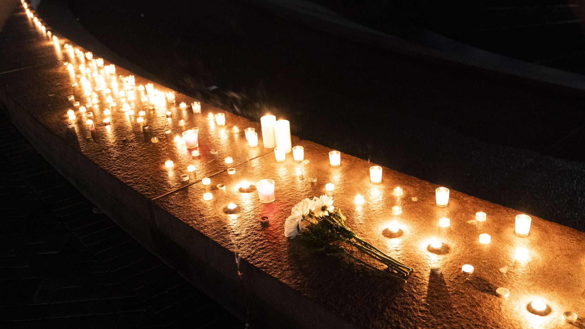A row of lit candles along a low wall to remember the victims of the Seattle Center shooting. 