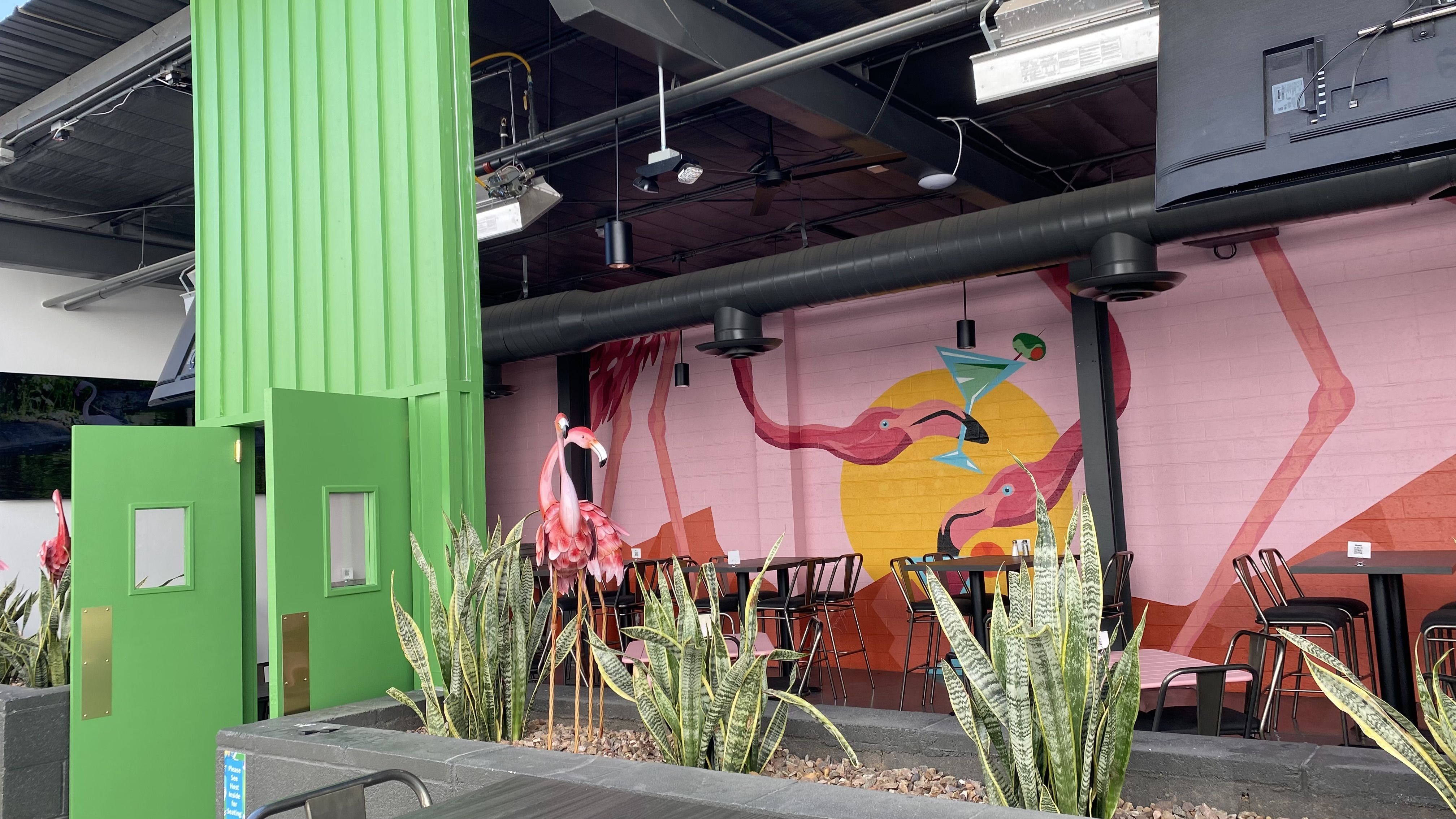 An outdoor bar with a mural depicting two flamingoes drinking from cocktail glasses. 