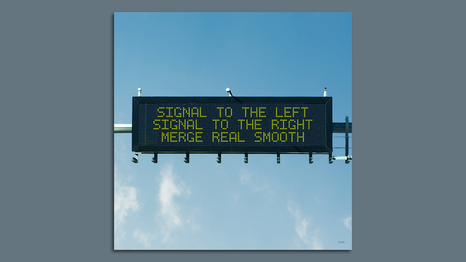 Electronic highway sign with yellow text on black background reading: "Signal to the left Signal to the right Merge real smooth" against a clear blue sky.