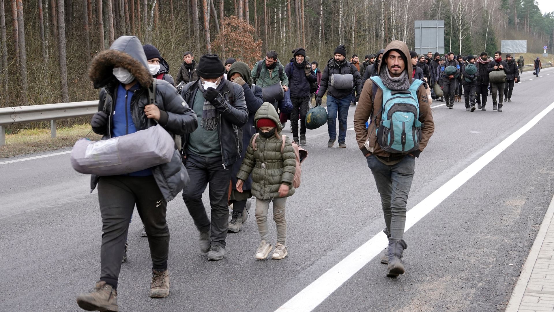 Migrants walk with their luggage to a warehouse near the border that has been set up as.