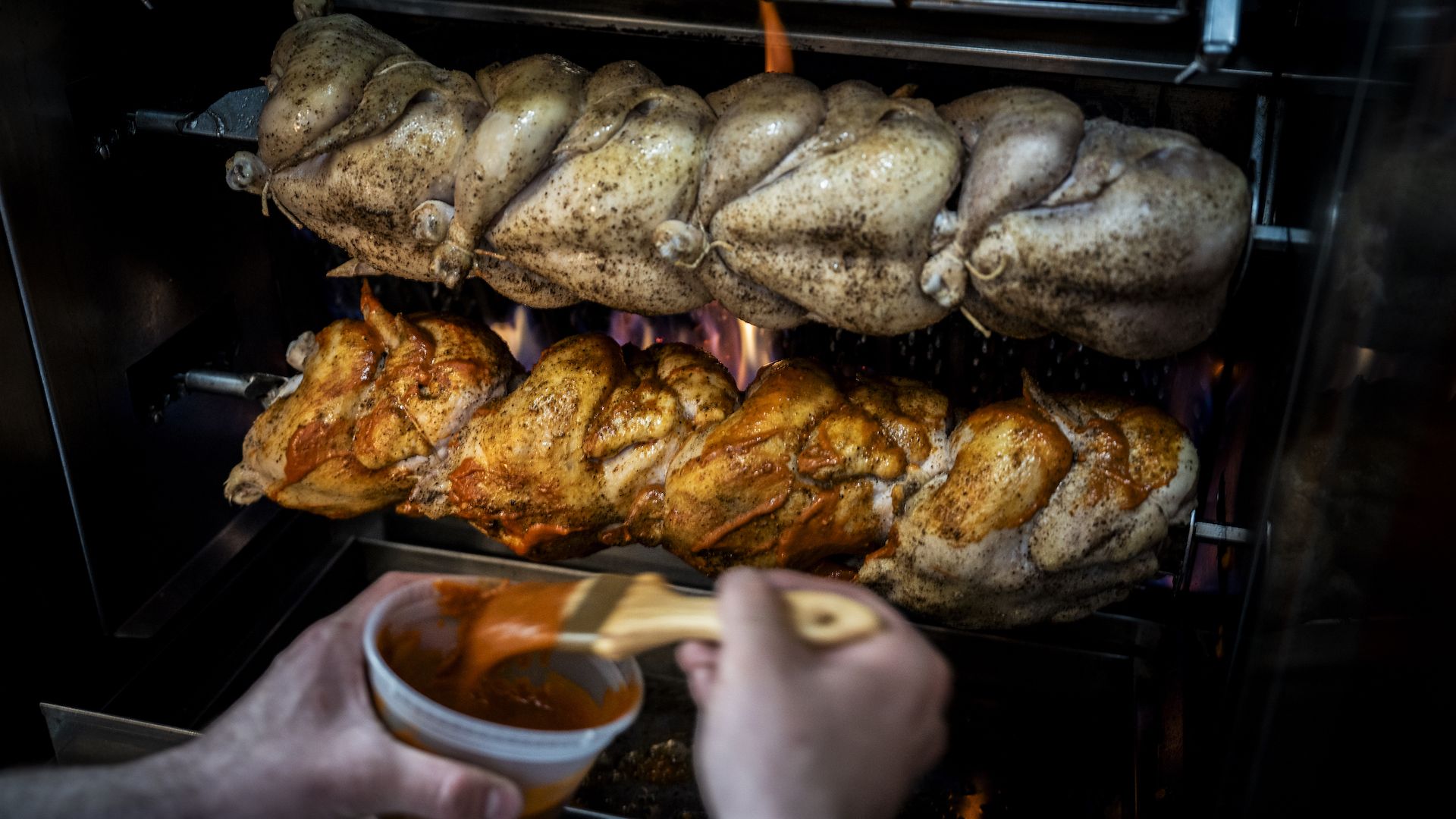 A chef puts sauces on rotisserie chickens on spickets.