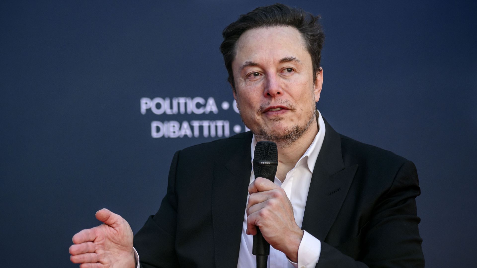 A photo of Elon Musk speaking into a microphone.