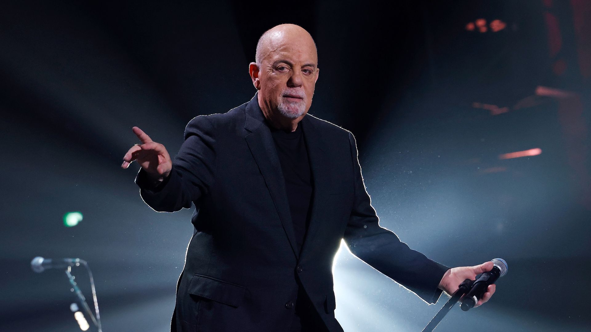 Billy Joel stands on stage with a microphone in his hand during a concert.