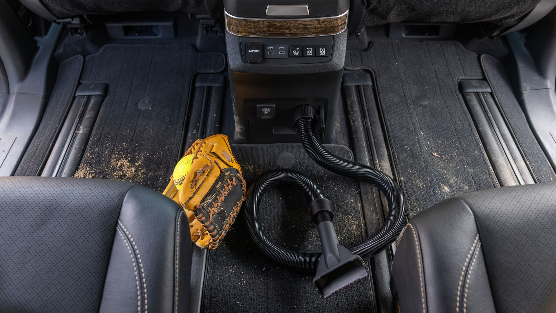 A vacuum attached to the back of a center console in a minivan, next to a kid's baseball glove