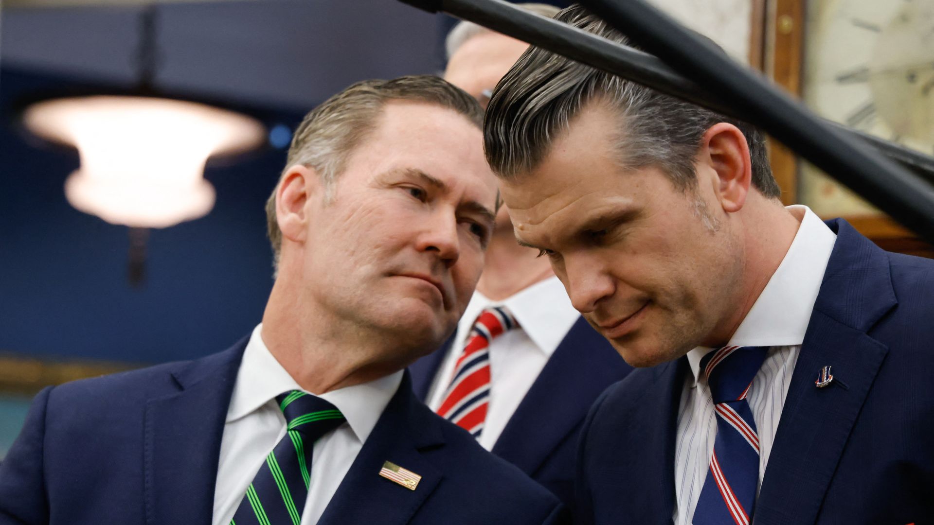 Mike Waltz and Pete Hegseth, both wearing blue suits and leaning into each other.
