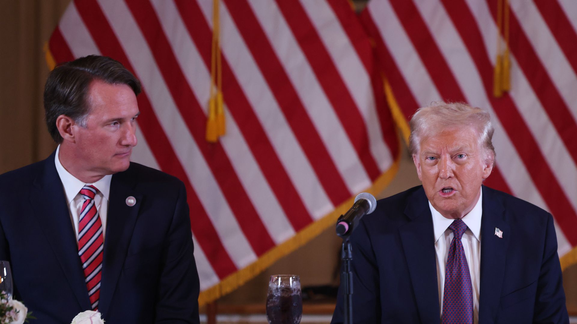 Trump and Youngkin sitting at a banquet table in front of an American flag