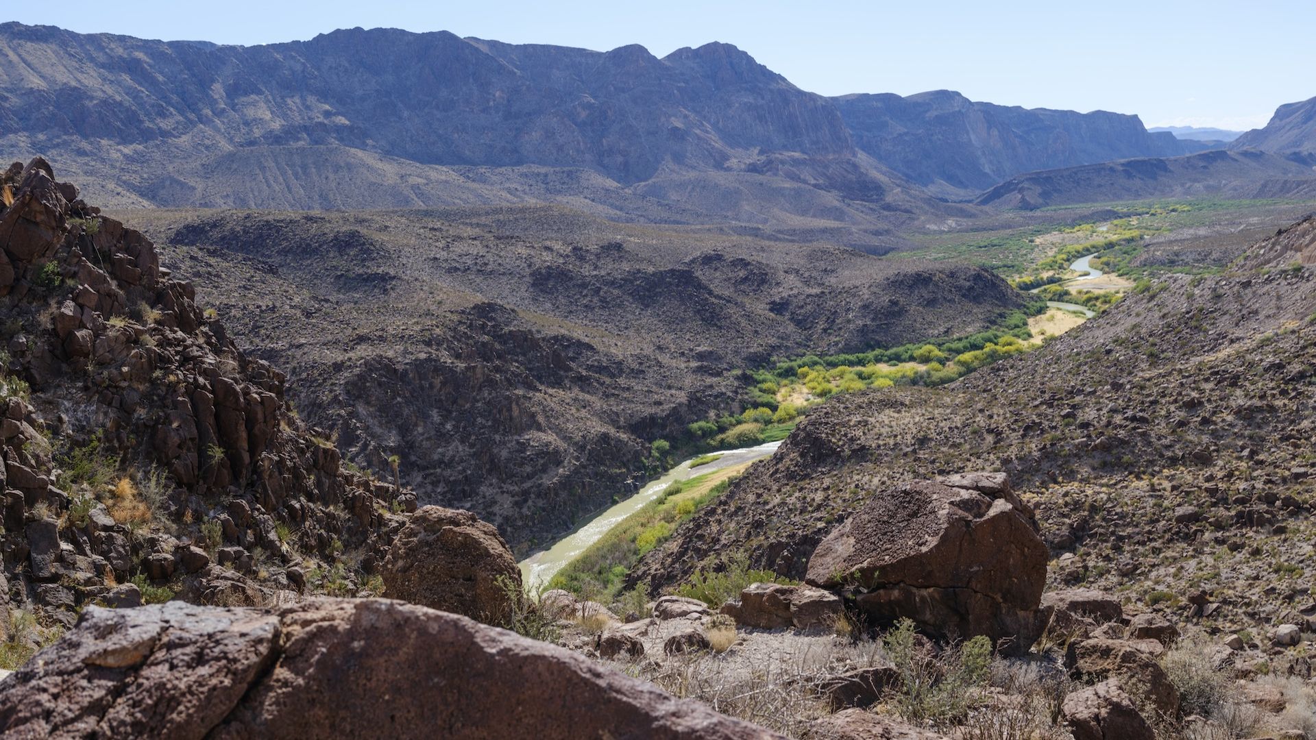 The Rio Grande River in Big Bend Ranch State Park in April. The small river is seen flowing through majestic mountains around it in a desert environment, with greenery surrounding only the river.