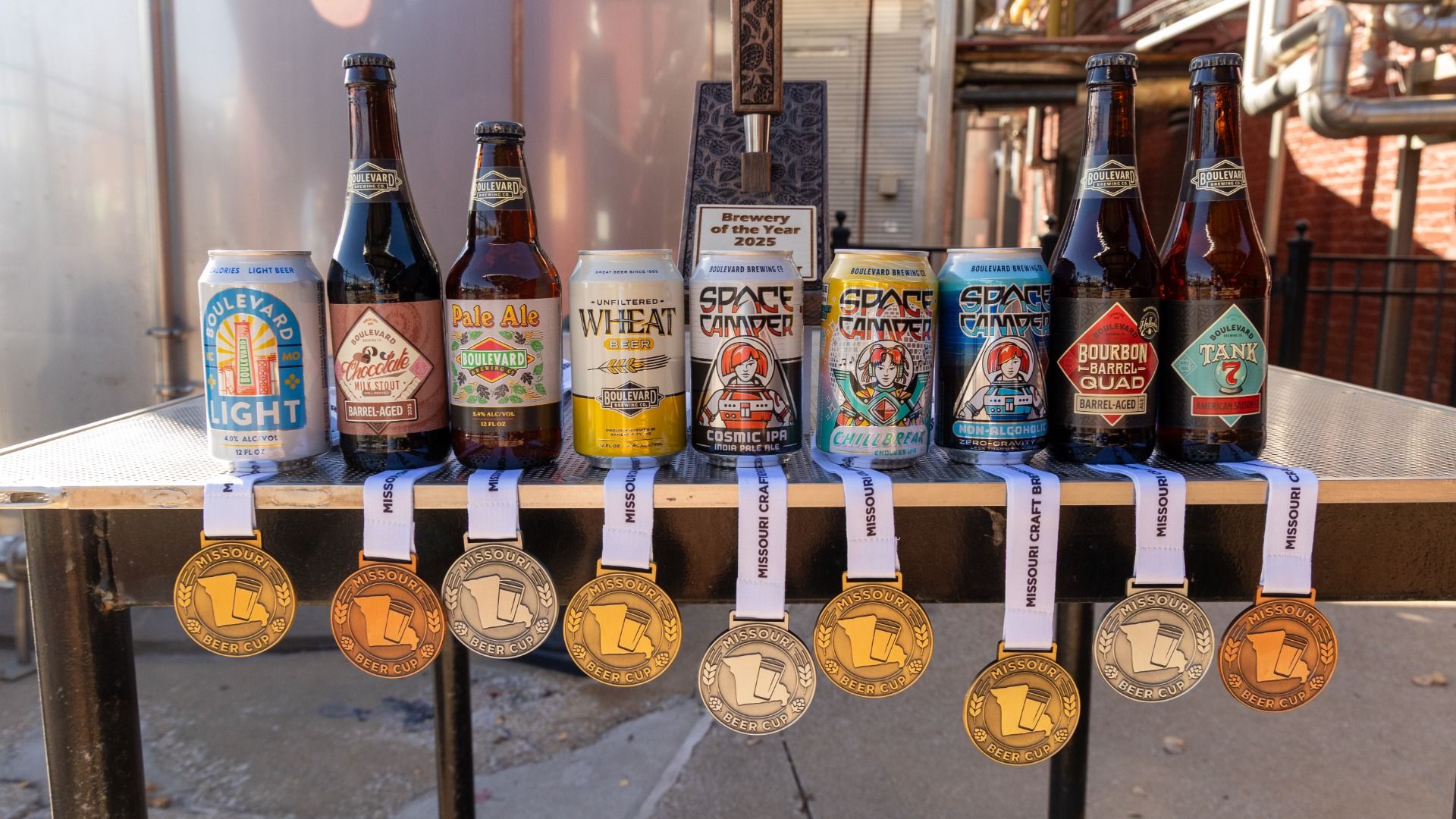 Nine bottles and cans of Boulevard Brewing Co. beer on a table with seven Missouri Beer Cup medals hanging from the table edge, including gold, silver, and bronze medals.