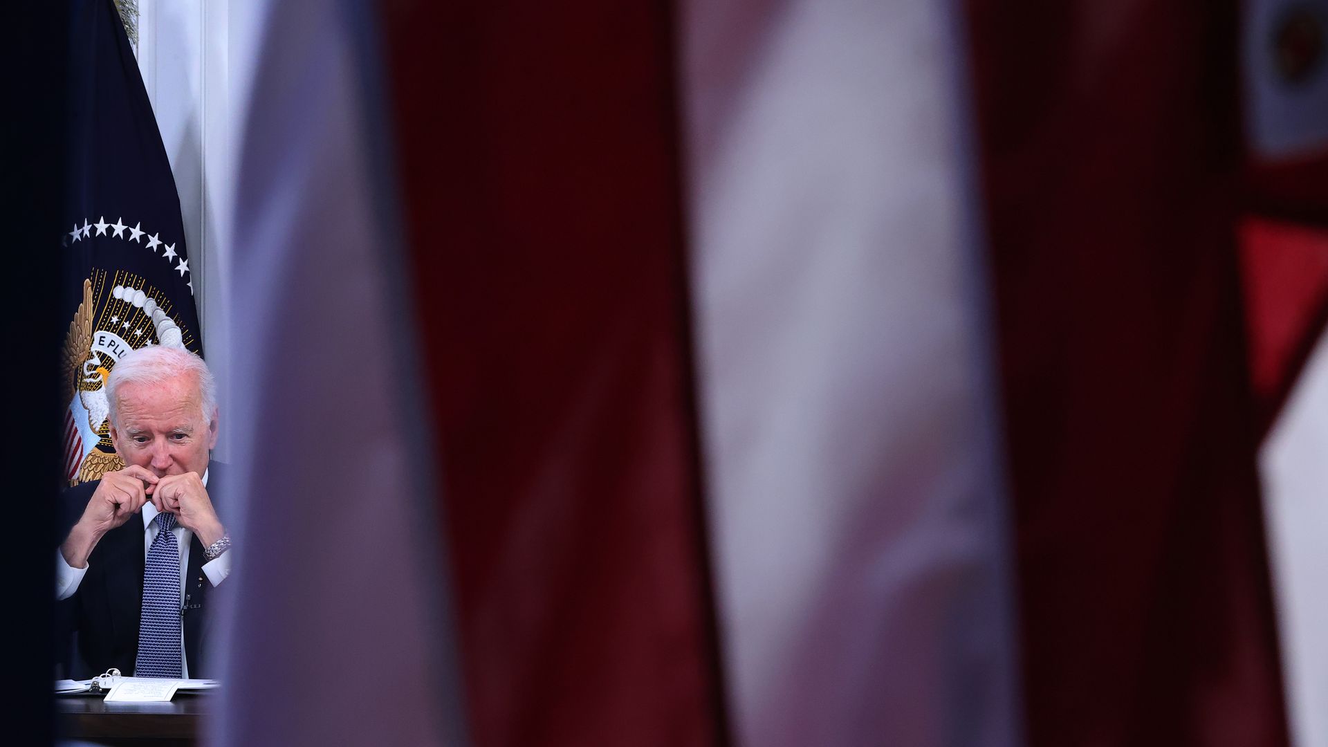 President Biden is seen between presidential and American flags.