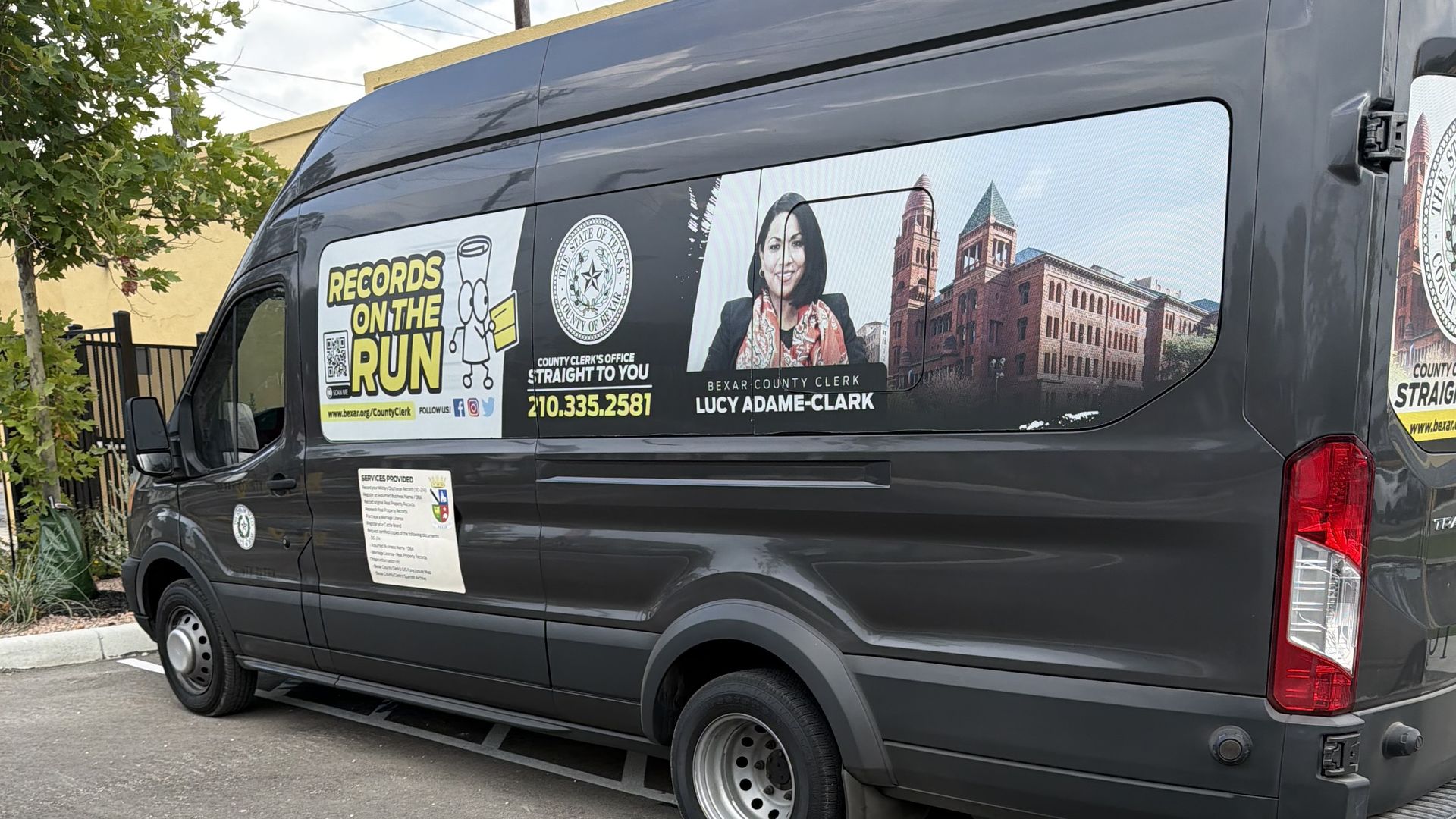 Side view of a dark gray van wrapped with promotional graphics, including the title "Records on the Run," a county seal, a photo of a female official, and brick courthouse imagery.