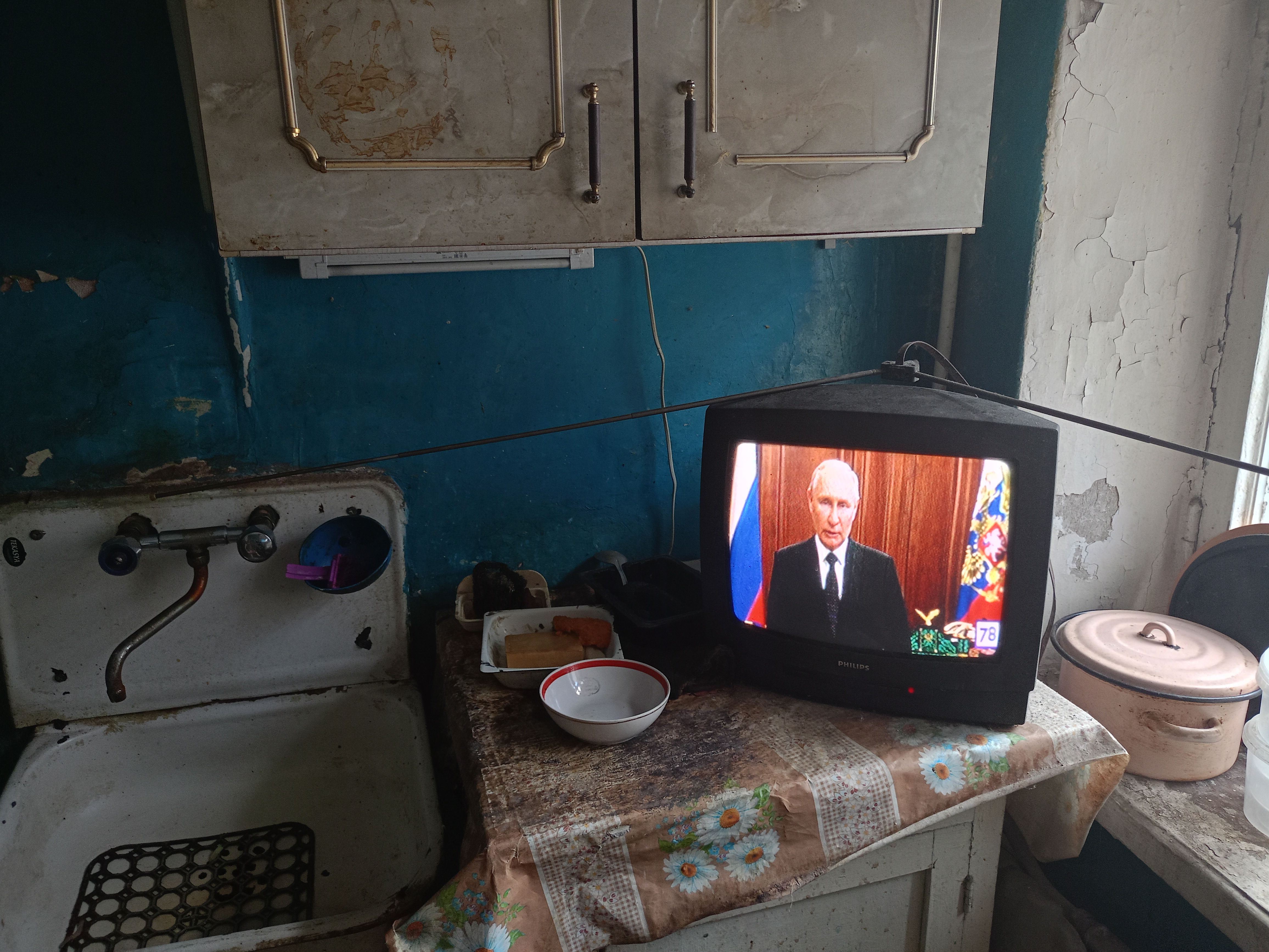 An image of a kitchen counter with a television showing Vladimir Putin making an appeal to the citizens of Russia. 