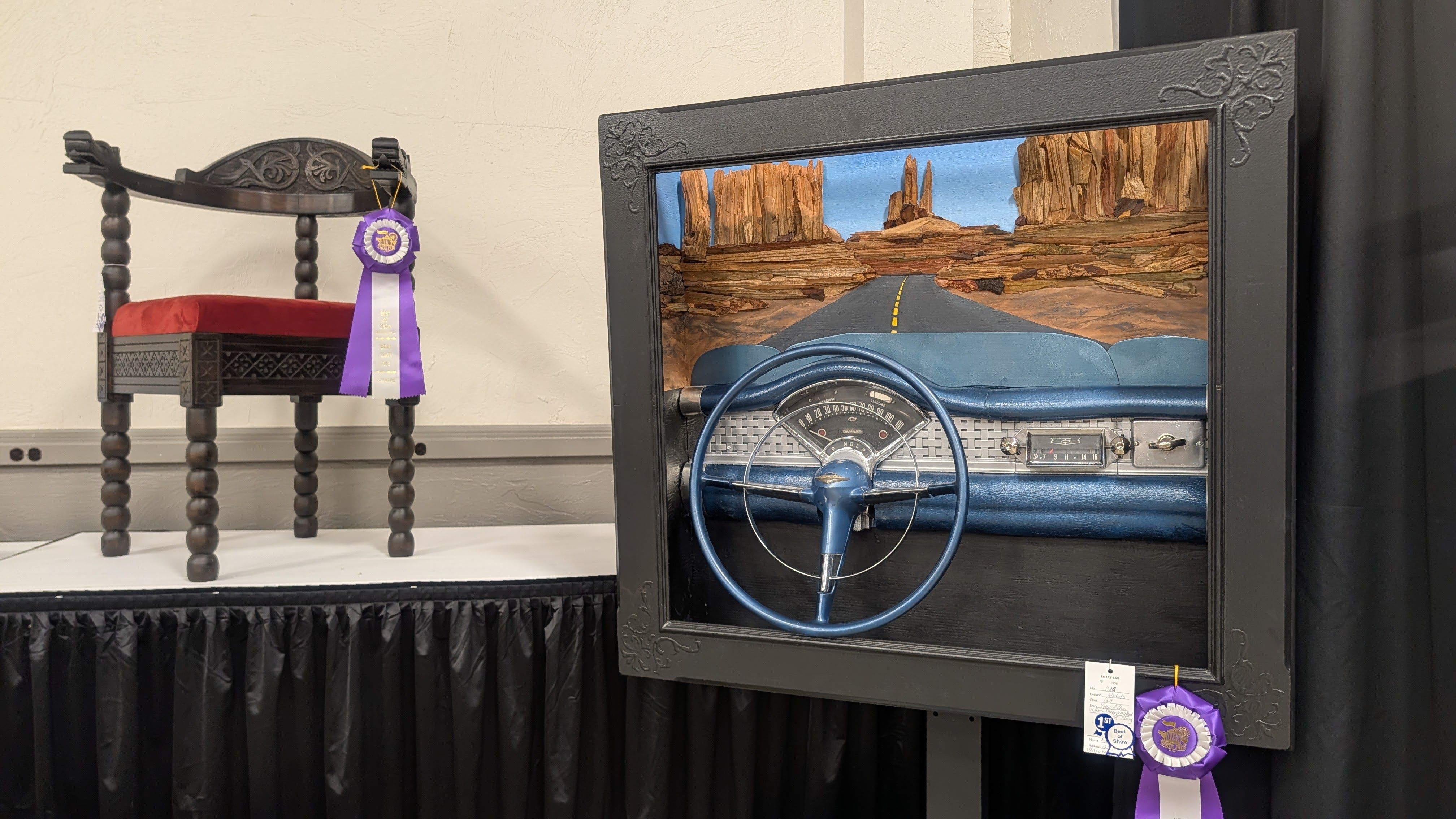 Left: carved dark wood chair with a red cushion and a purple ribbon award. Right: framed desert road diorama with a blue vintage car dashboard, a yellow centerline, and towering orange rock formations.