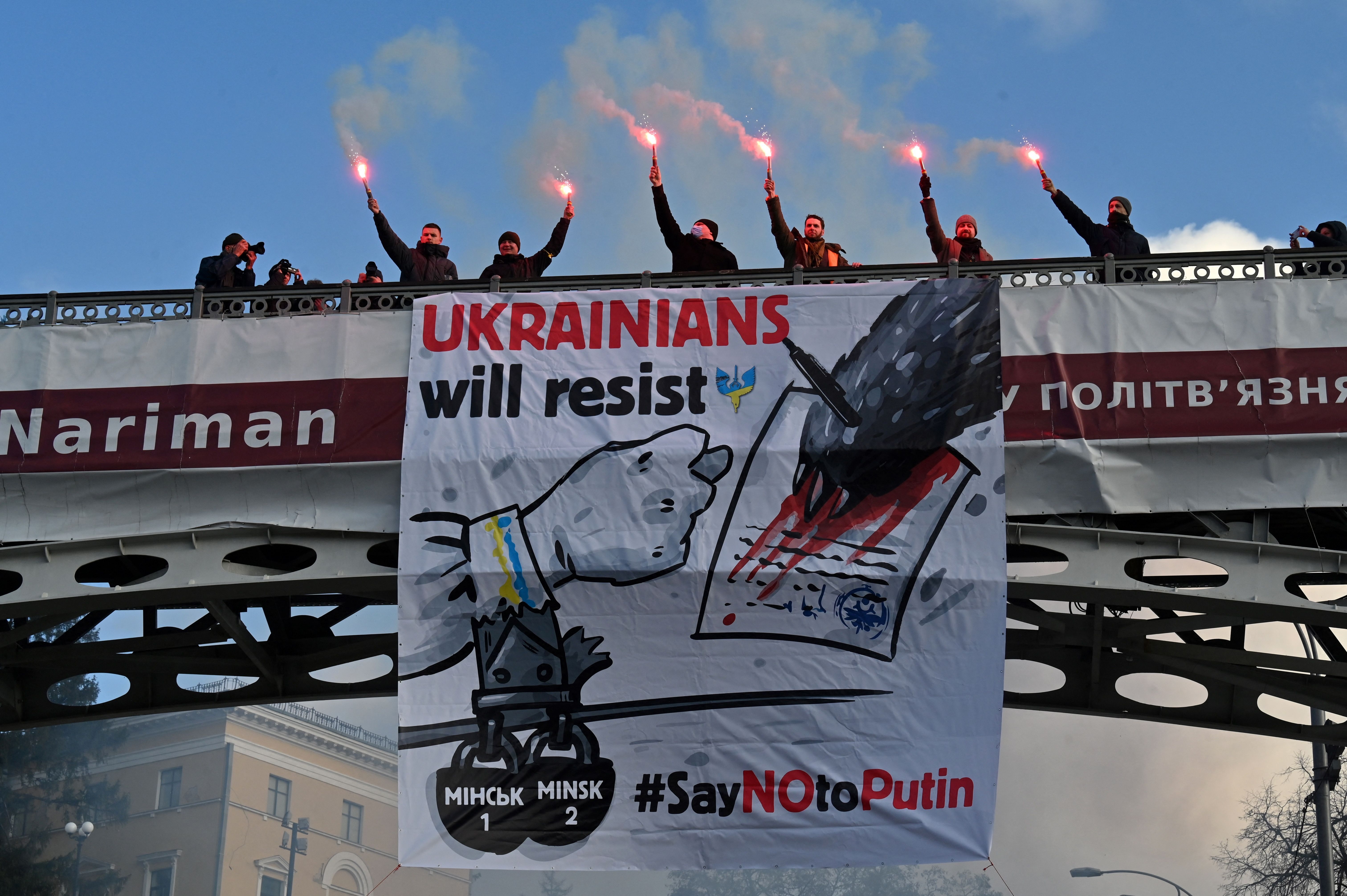 Demonstrators shout slogans as they stand with lit flares on a bridge adorned with a banner 'Ukranians will resist - Say No to Putin' during a rally in Kyiv on February 12, 2022.