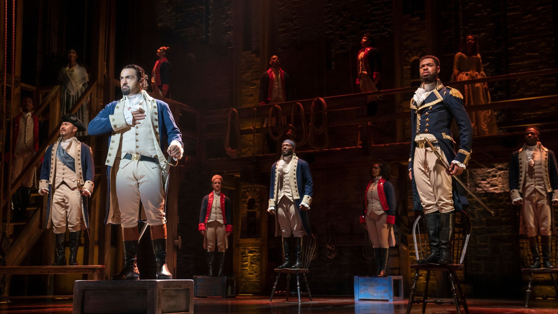 A scene from "Hamilton" the musical on a stage. People are dressed as revolutionary war characters.