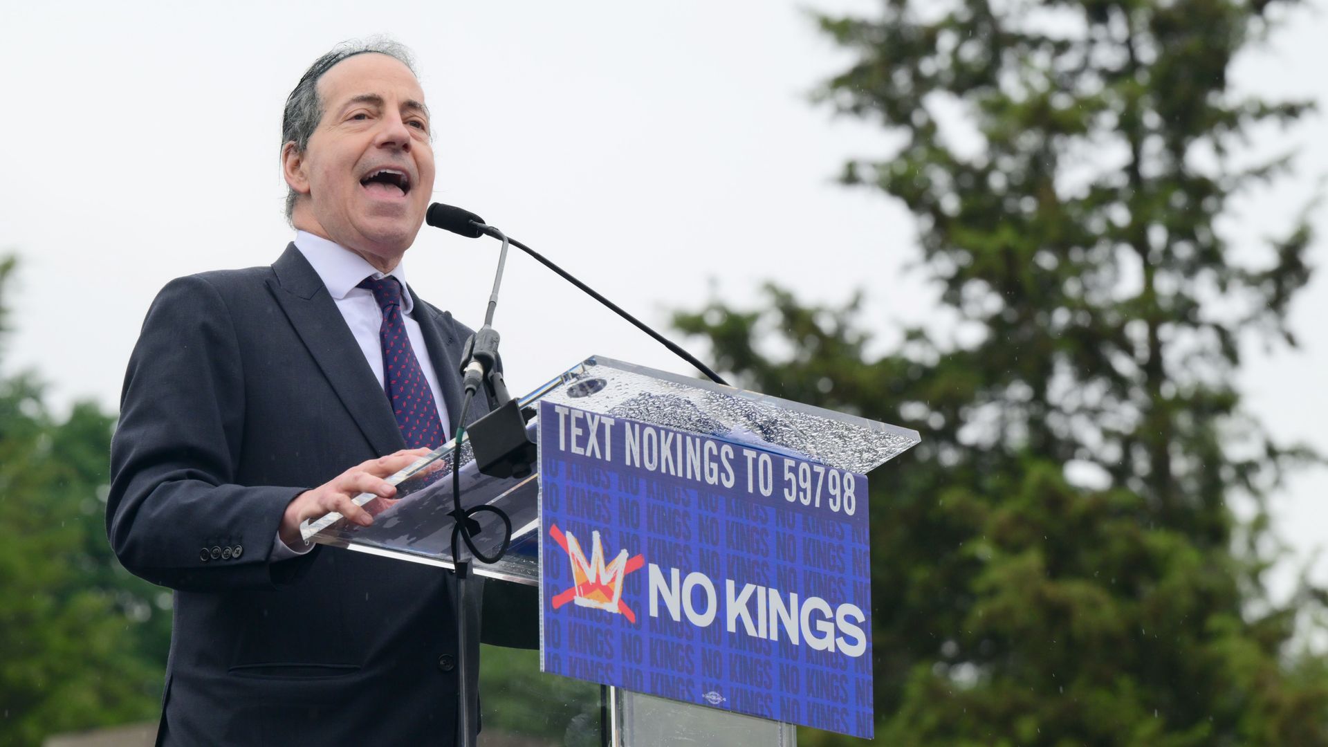 Jamie Raskin, wearing a dark suit, speaks at a "No Kings" rally from behind a podium.