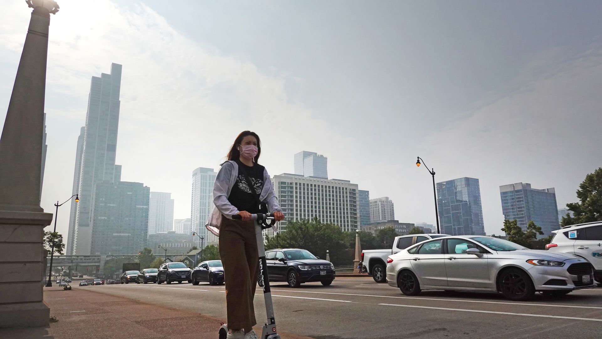 A person wearing a mask while riding a scooter as a smokey haze fills the air in downtown Chicago on June 28.