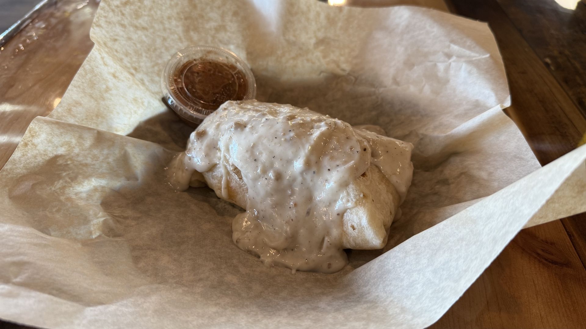 A burrito smothered in sausage gravy in a basket lined with wax paper. 