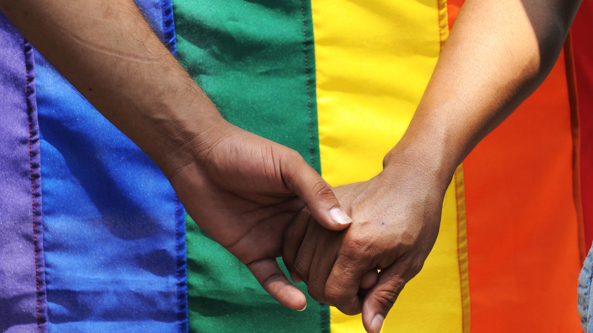 Two hands are held together in front of a pride flag