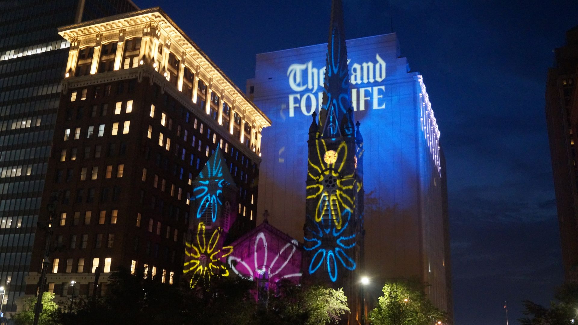 A light display projects multicolored daisies on an old stone church at night.