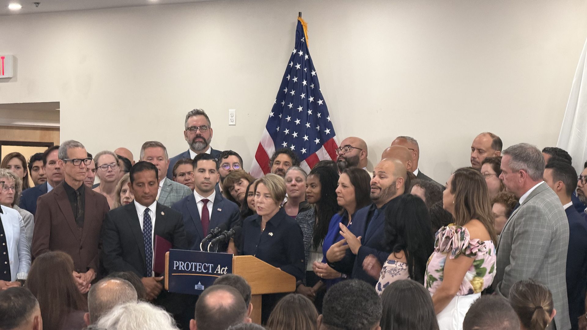 Gov. Maura Healey, surrounded by lawmakers and advocates, addresses hundreds packed into La Colaborativa in Chelsea before signing an immigrant protections bill into law on Aug. 5, 2026.