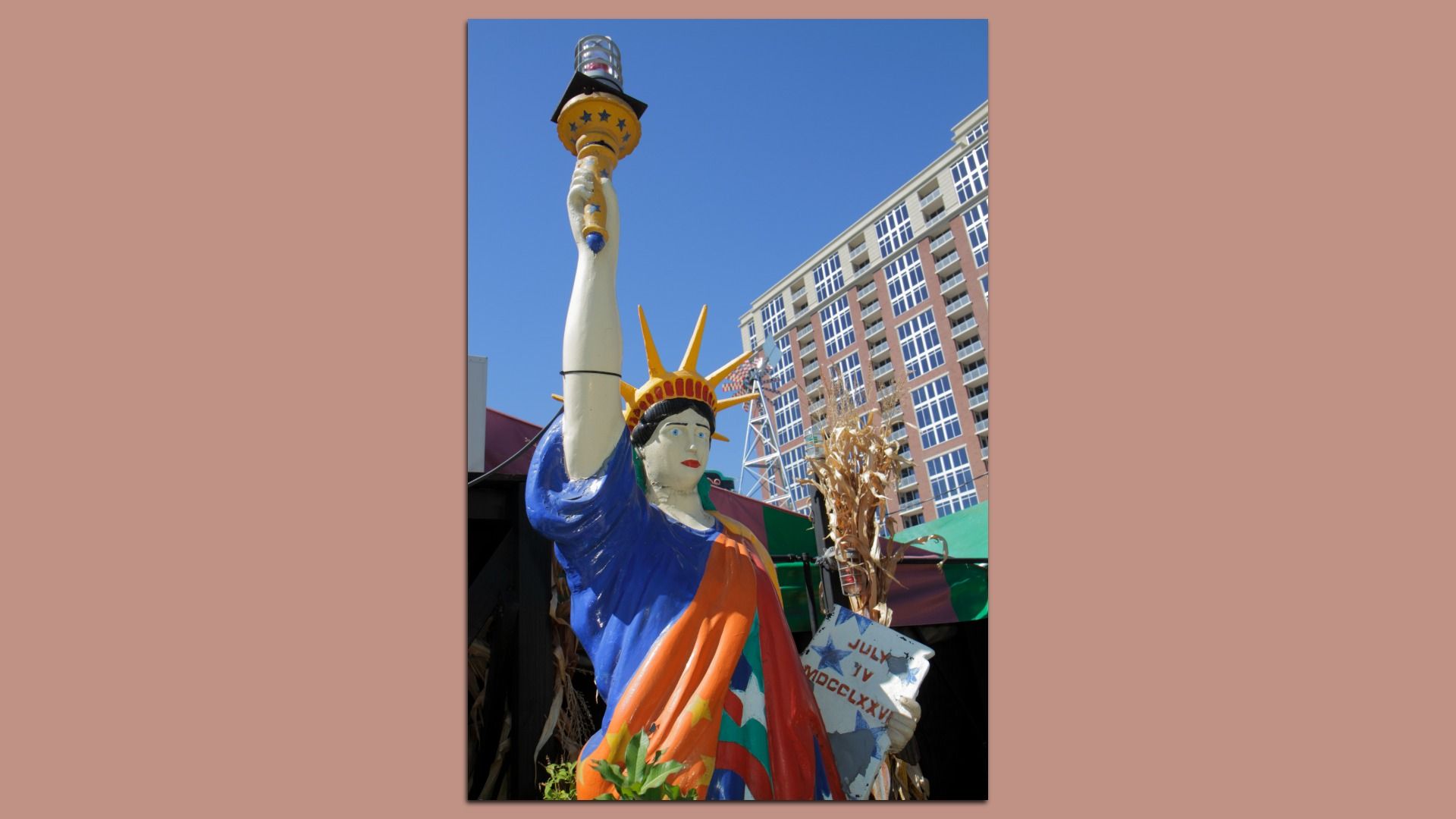 A photo of a colorful painted recreation of the Statue of Liberty standing in front of a funky restaurant next door to a high-rise residential building