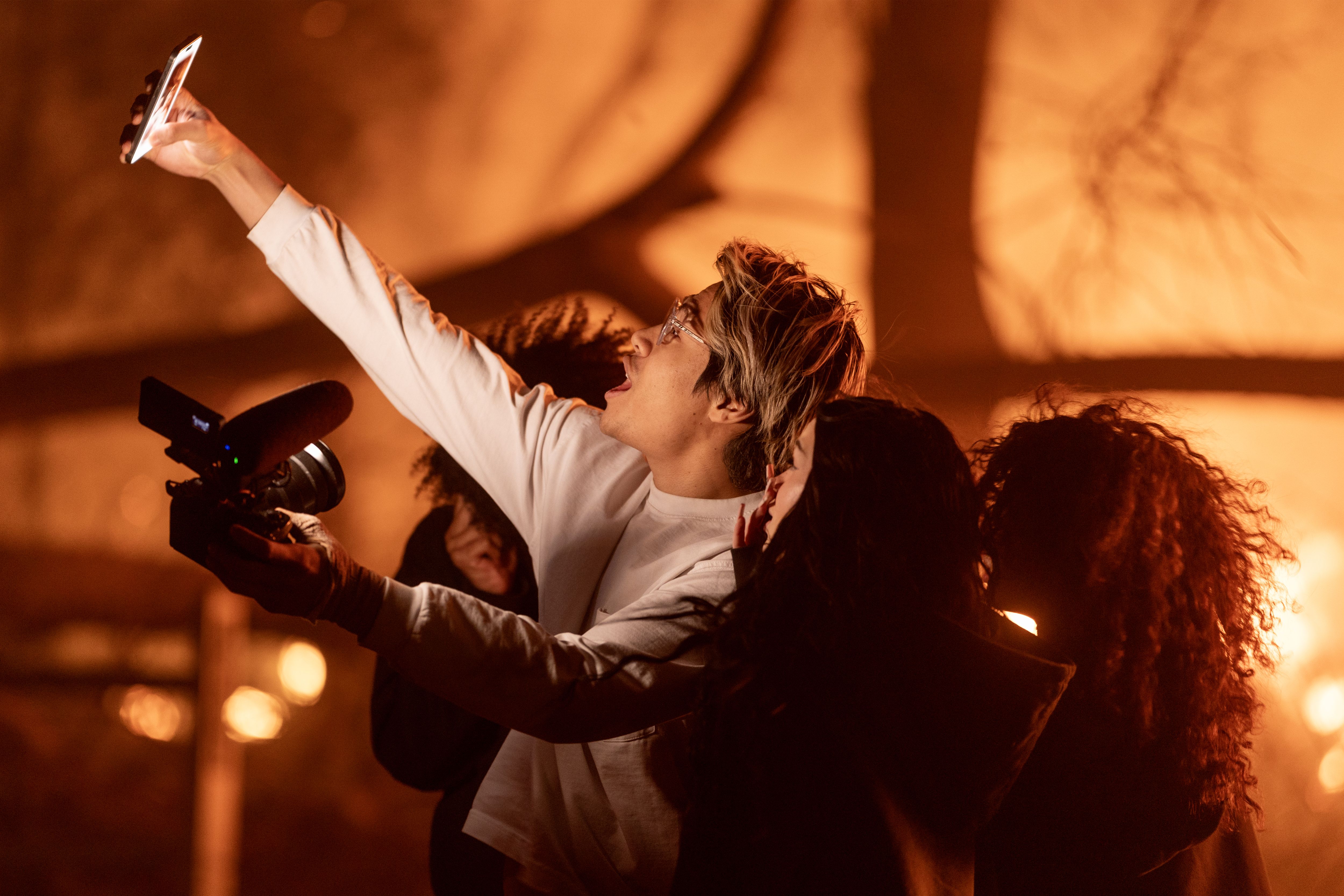 Young people holding up phones to take selfies while a fire burns in the background. 