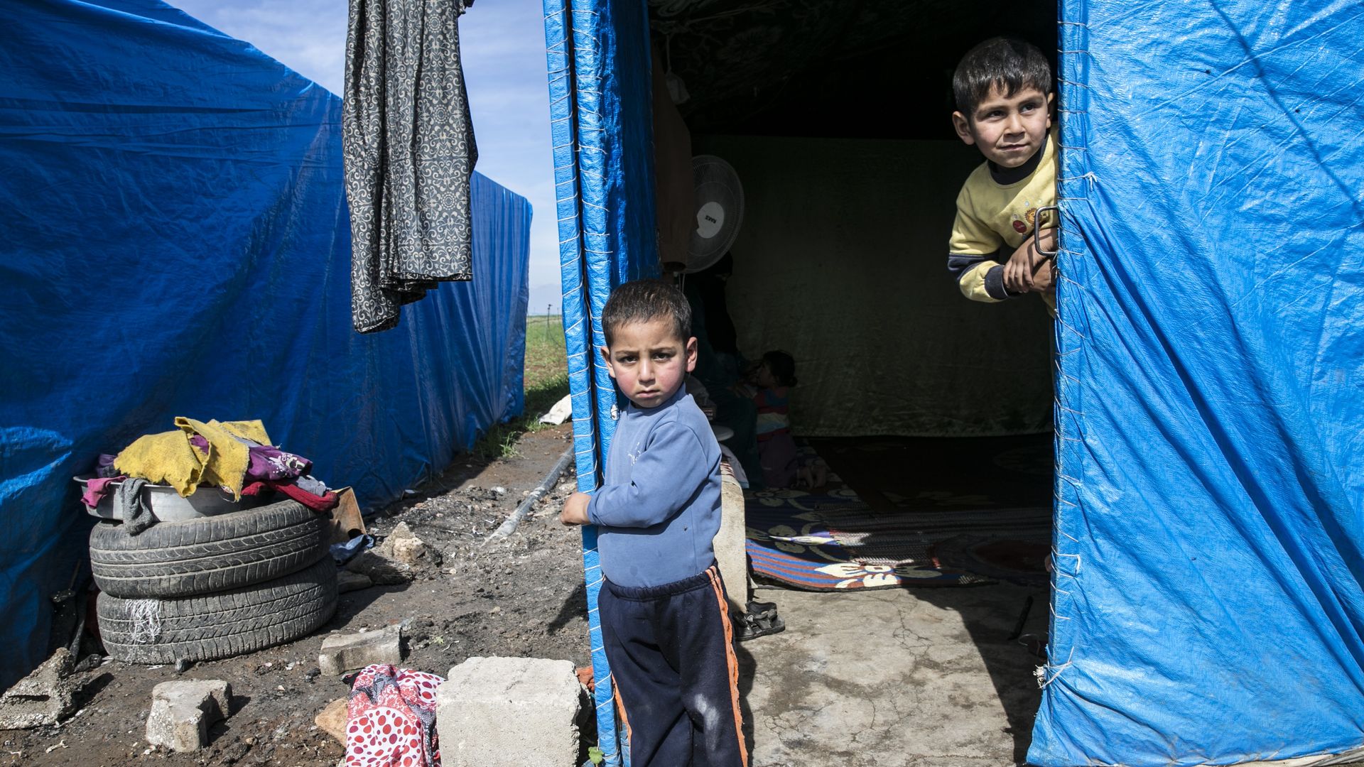 Syrian children next to a tent in a refugee camp
